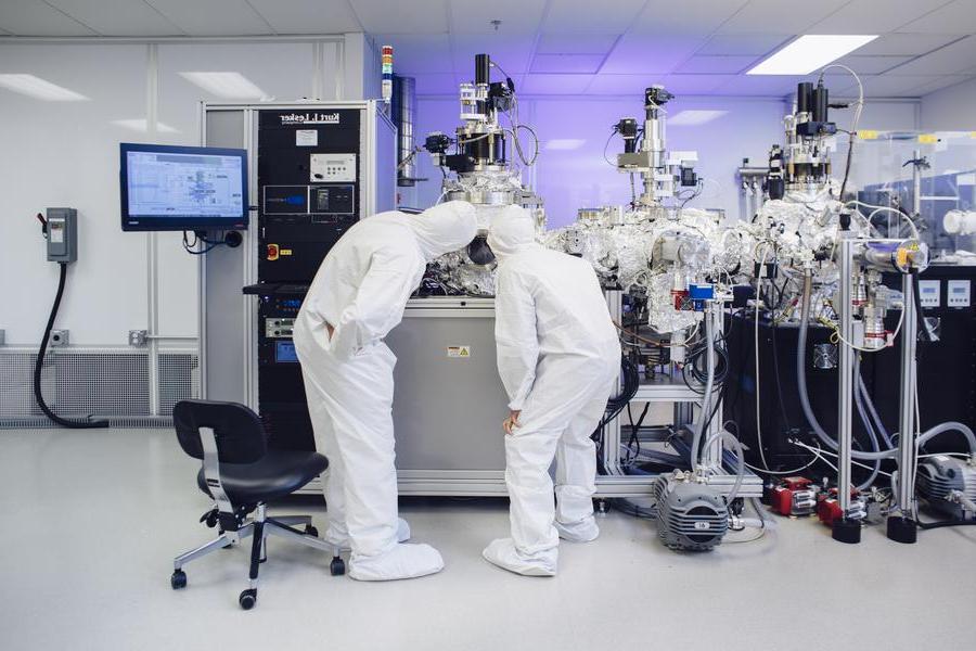 两名科学家穿着白色连体衣在一间洁净室里观察和实验.